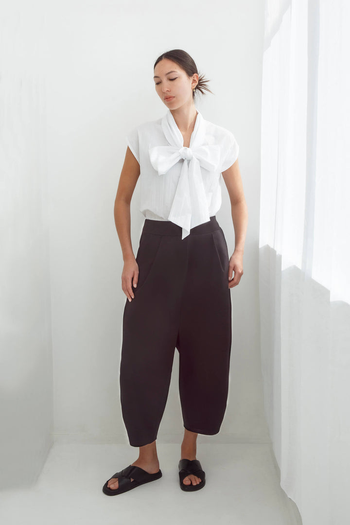 Woman wearing a white pleated sleeveless handmade top and japanese pants against a white background