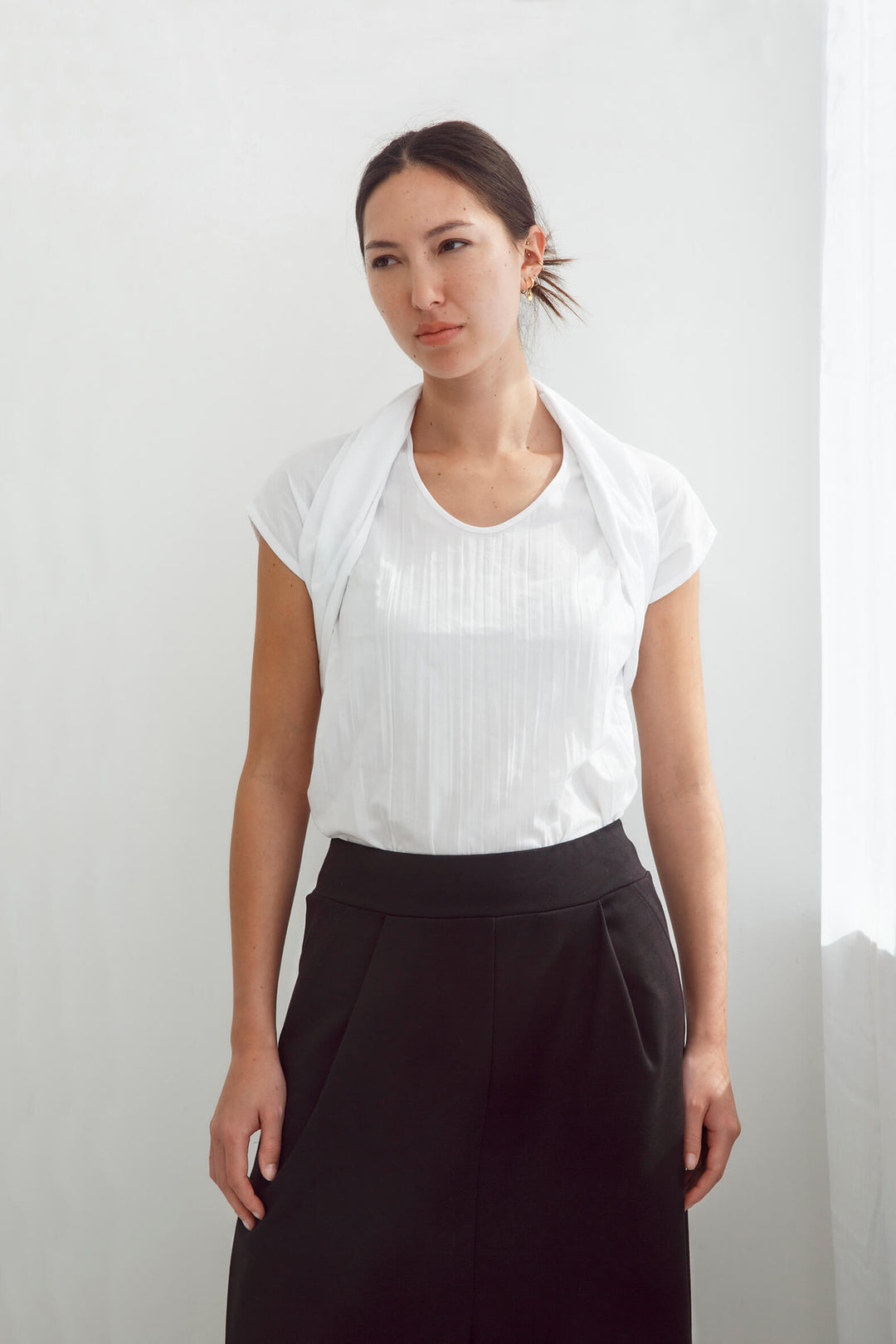 Woman wearing a handmade pleated japanese white sleeveless top with a big bow tie and black pants against a white background