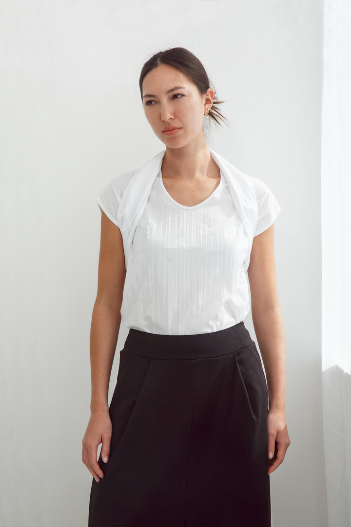 Woman wearing a handmade pleated japanese white sleeveless top with a big bow tie and black pants against a white background