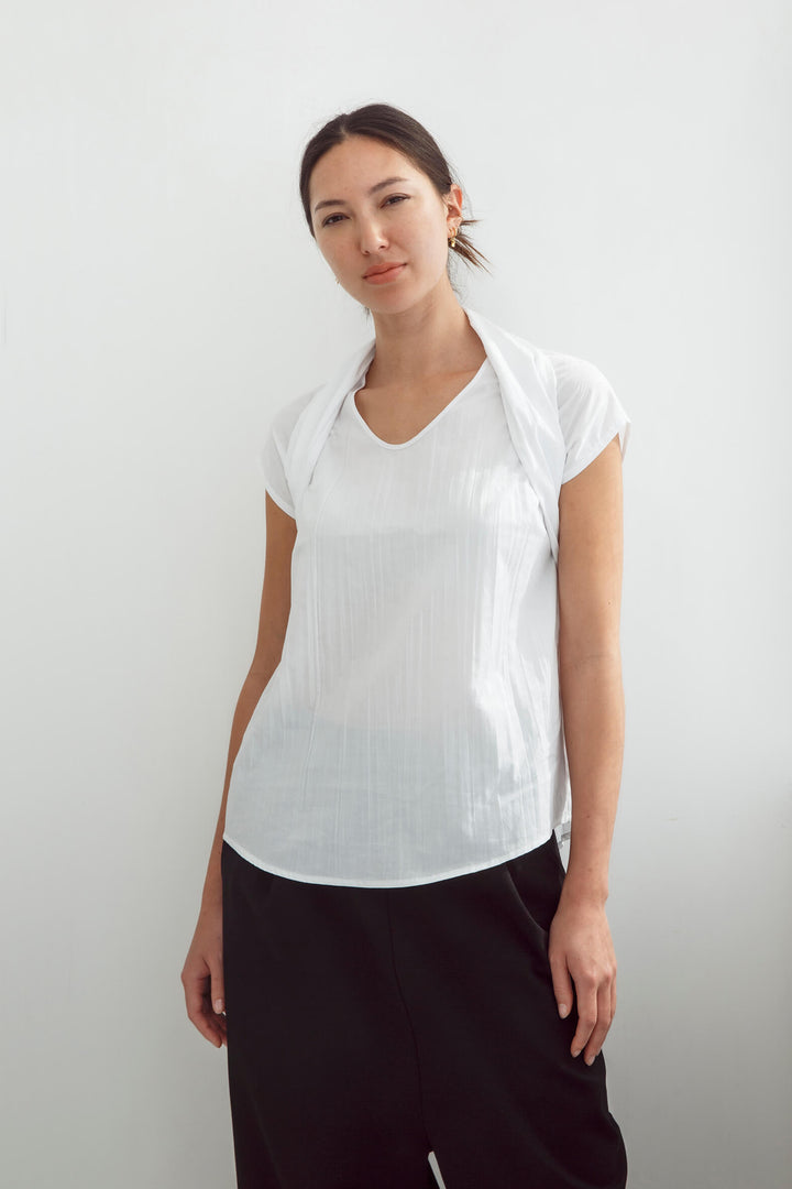 Woman wearing a handmade pleated japanese white sleeveless top with a big bow tie and black pants against a white background