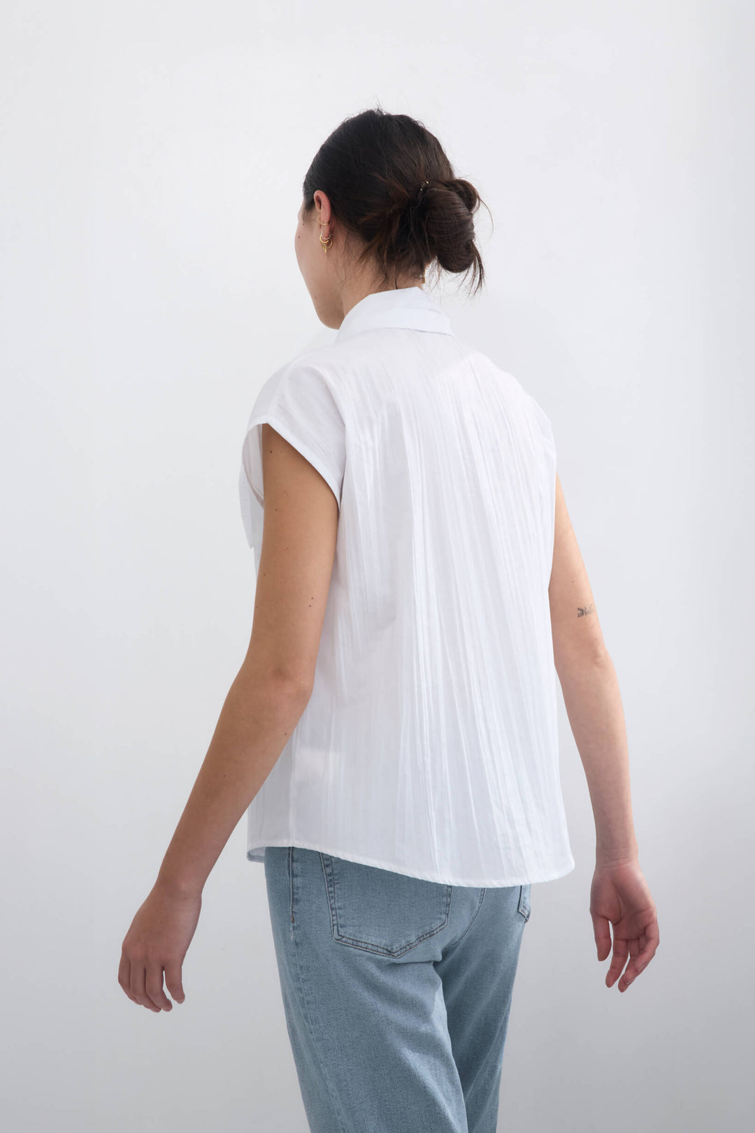 Woman wearing a handmade pleated japanese white sleeveless top with a big bow tie and jeans against a white background