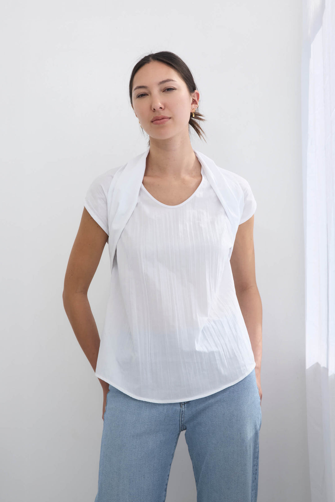 Woman wearing a handmade pleated japanese white sleeveless top with a big bow tie and jeans against a white background
