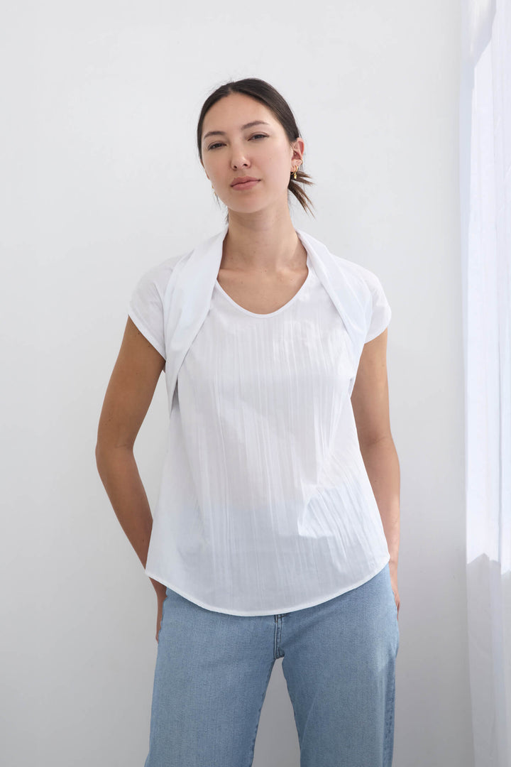Woman wearing a handmade pleated japanese white sleeveless top with a big bow tie and jeans against a white background